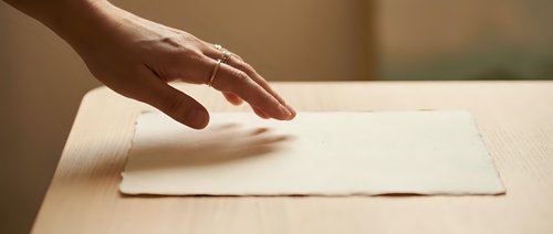 Woman's hand reaching toward blank white envelope on wooden table, suitable for business correspondence and mail concepts.