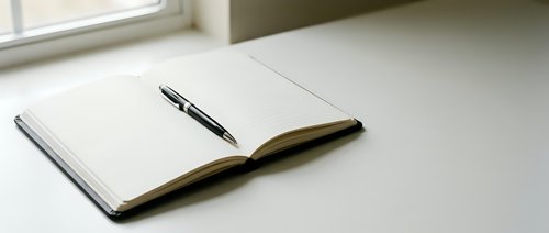 Open notebook with black pen on white desk near window for writing planning journaling office workspace productivity business education study notes.