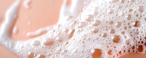 Macro shot of soap foam bubbles in soft pink and white tones creating abstract texture pattern with water droplets and light reflections. For beauty and hygiene concepts.