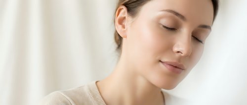 Young Caucasian woman with closed eyes in peaceful meditation pose wearing beige clothing in soft natural light for wellness and mindfulness concepts.