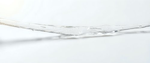 Clear water stream flowing dynamically across white surface, suitable for beverage, wellness, and product advertising campaigns.