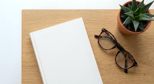 Blank white notebook with eyeglasses and succulent plant on wooden desk surface for office workspace mockup and business planning concepts.