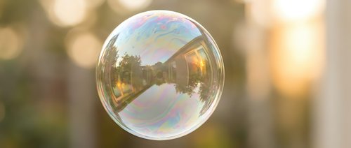 Single soap bubble floating in air with rainbow iridescent surface reflecting warm sunlight and blurred bokeh background for dreamy atmospheric concepts.