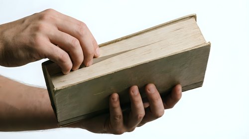 Male hands holding thick vintage book with worn green cover and aged pages on white background for educational and literary projects.