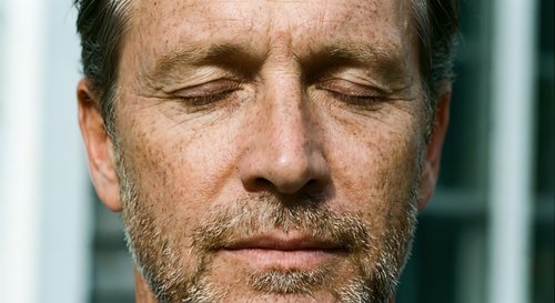 Middle-aged Caucasian man with closed eyes and beard in peaceful meditation pose showing mindfulness and relaxation for wellness content.