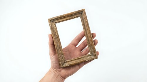 Hand holding empty wooden picture frame against white background for mockup and design projects.