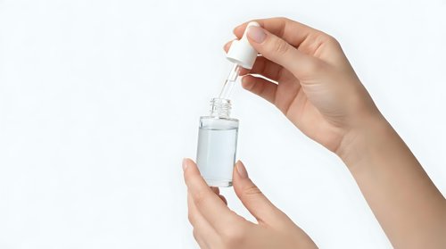 Woman hands applying clear serum from glass dropper bottle on white background. Skincare routine, cosmetic treatment, beauty product application.