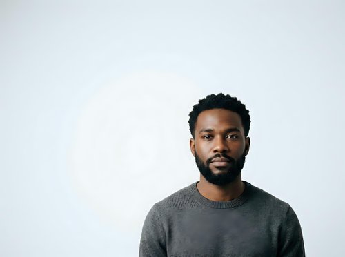 Young African American man with dark curly hair and beard wearing gray crew neck sweater against white background, suitable for corporate portraits, professional headshots, and business website use.