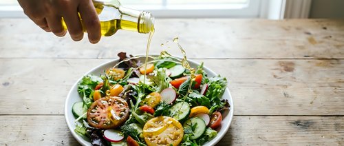 Drizzling olive oil over fresh salad with grilled vegetables, lemon slices, and greens on wooden table for healthy eating and cooking.