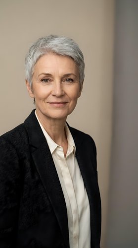 Senior woman with short gray hair, Caucasian ethnicity, wearing black blazer and white shirt. Professional business portrait for corporate, executive, and leadership applications.