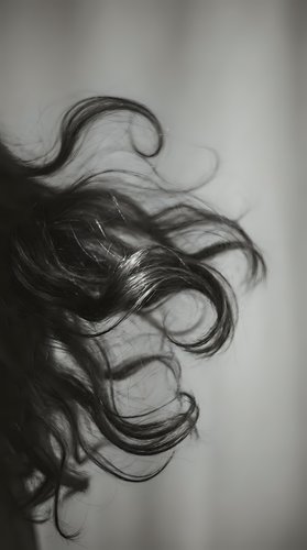 Flowing dark hair strands in motion captured in artistic black and white photography with soft focus and elegant movement for beauty and fashion concepts.