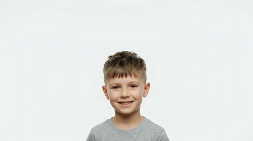 Portrait of a young boy with light brown hair and fair complexion, wearing a gray t-shirt, smiling at camera against neutral background for stock photography.