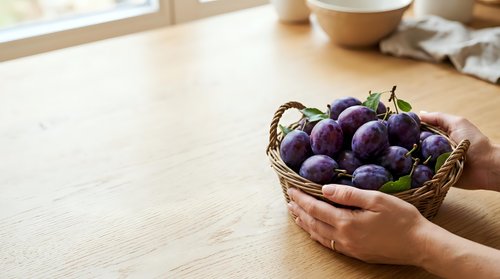 Fresh purple eggplants in wicker basket held by hands on wooden table with natural light, suitable for food, cooking, and agricultural content.