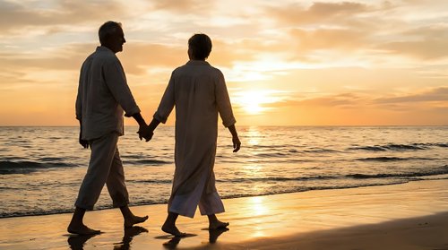 Romantic couple holding hands walking on beach at golden sunset with ocean waves and dramatic sky creating peaceful moment for love and relationship concepts.
