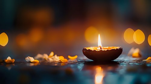 Burning diya lamp with soft bokeh lights and flower petals in dark background, traditional spiritual celebration atmosphere for meditation and mindfulness.