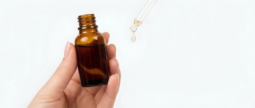 Hand holding amber glass dropper bottle with pipette dispensing liquid drop isolated on white background for skincare cosmetics packaging design.