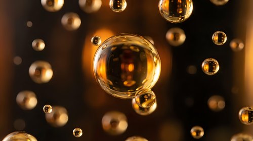 Golden oil bubbles floating in dark liquid creating abstract luxury cosmetic background with warm lighting effects.