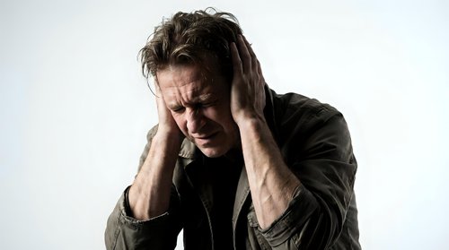 Stressed middle-aged Caucasian man holding head in hands experiencing severe headache or migraine pain against neutral background for health concepts.