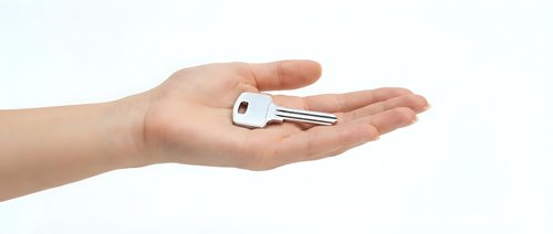 Female hand holding silver house key on open palm against white background, real estate concept for new home ownership and property investment.