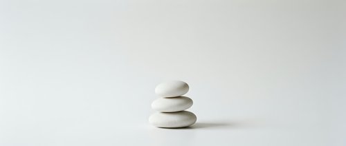 Three smooth white zen stones balanced in minimalist stack on clean background for meditation wellness spa design concepts.