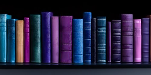 Row of vintage hardcover books in blue and purple shades standing on dark shelf against black background, creating minimalist library atmosphere.