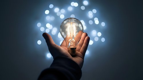 Hand holding glowing vintage light bulb with bokeh lights background representing innovation creativity and bright ideas for business solutions.