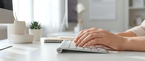 Female hands typing on white wireless keyboard at modern office desk with laptop and succulent plant in bright workspace for productivity and business.