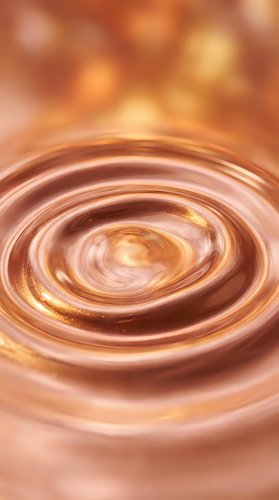 Concentric swirling liquid ripples in warm copper and gold tones create an abstract vortex effect, suitable for backgrounds and design projects.