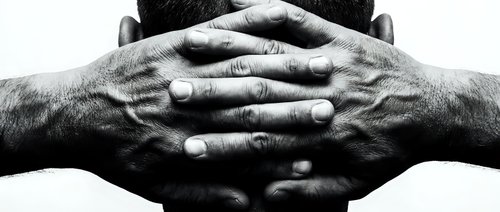 Mature businessman hands clasped behind head in contemplative pose, black and white portrait showing confidence and decision-making in corporate environment.