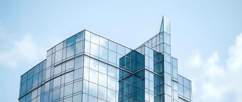 Modern glass office buildings with reflective facades against blue sky with white clouds creating contemporary urban architecture for business concepts.