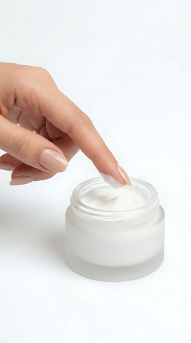 Female hand with light skin tone applying white moisturizing cream from glass jar for skincare, cosmetics, beauty, and wellness product advertising.