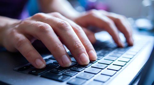 Professional hands typing on modern laptop keyboard in office environment with soft lighting and technology workspace background.