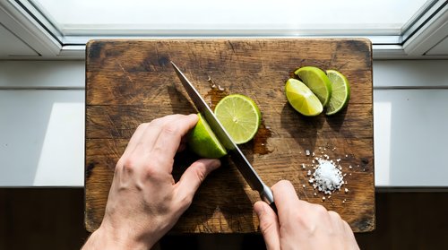 Chef's hands holding knife and lime on wooden cutting board with sea salt and chopsticks for cooking, food preparation, and culinary design projects.