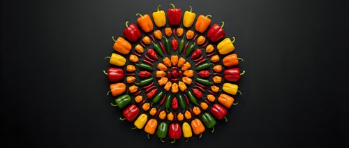 Colorful bell peppers arranged in circular mandala pattern on dark background for healthy eating and vegetarian cooking concepts.