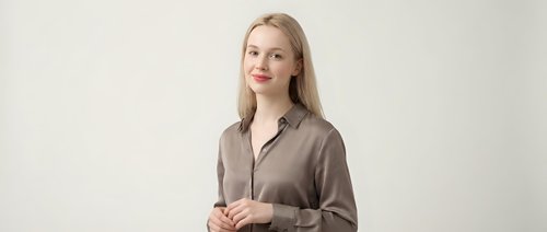 Young blonde Caucasian businesswoman in brown blazer standing confidently against neutral background for corporate presentations and marketing materials.