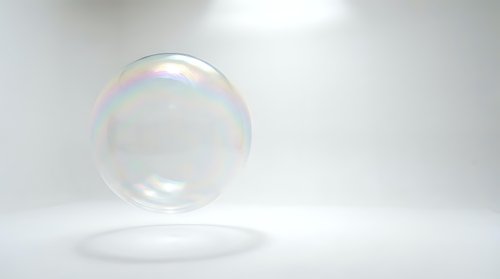 Single transparent soap bubble floating above white surface with rainbow iridescent reflections and soft lighting for clean minimalist design concepts.