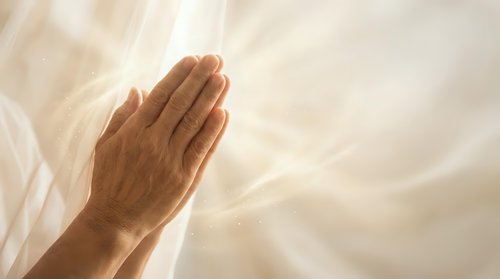 Hands pressed together in prayer position against soft flowing white fabric background creating peaceful spiritual atmosphere for meditation and worship.