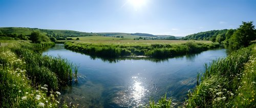 Scenic river landscape with lush green vegetation, rolling hills, and clear blue sky reflecting in calm water, suitable for nature and travel content.