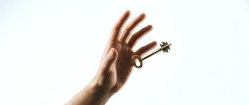 Hand holding vintage brass key against bright light creating dramatic silhouette effect for success and opportunity concepts in business presentations.