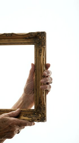 Elderly hands holding ornate golden picture frame on white background, isolated for design projects and creative artwork displays.