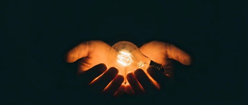 Hands holding glowing orb of light against dark background, symbolizing innovation, energy, power, and shared vision for business and technology concepts.