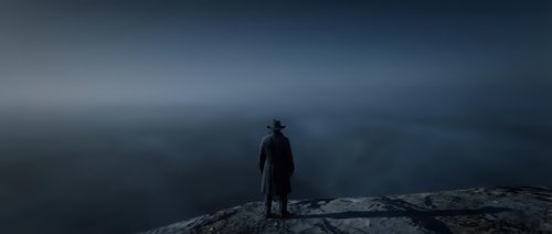 Man in dark coat standing alone on rocky mountain peak overlooking misty valley landscape at dusk. Solitude and contemplation concept for editorial and lifestyle use.