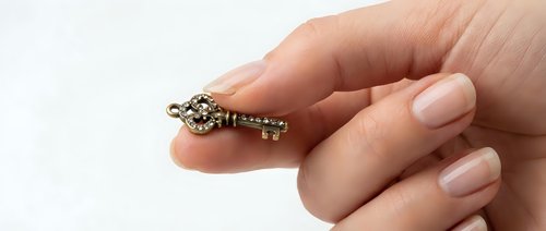 Hand holding vintage brass ornate key between fingers on white background for security and access concepts.