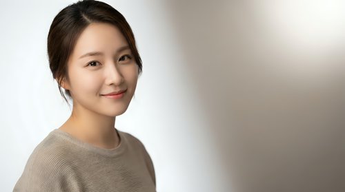 Young Asian woman smiling warmly in casual beige sweater against soft neutral background for lifestyle and portrait photography projects.
