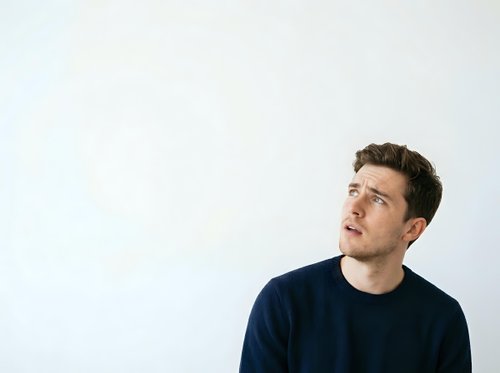 Young adult male, Caucasian ethnicity, wearing dark navy casual shirt, looking upward thoughtfully against white background, isolated portrait suitable for business, lifestyle and editorial design projects.