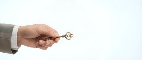 Businessman hand holding golden key against white background, symbolizing success, opportunity, solution, and unlocking potential for business concepts.