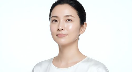 Young Asian woman with natural makeup and pulled back hair wearing white shirt on clean background for skincare and beauty concepts.