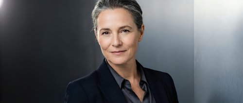 Professional mature businesswoman with gray hair in black suit jacket against modern gradient background for corporate presentations and leadership concepts.
