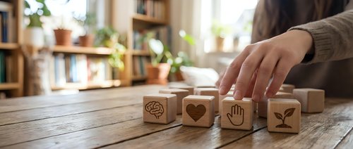 Woman arranging wooden blocks with carved symbols on rustic table in cozy home office setting with plants and books in background.