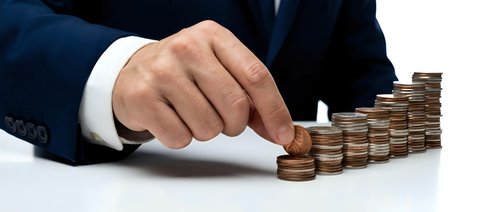 Male hand in business suit pushing stack of coins, representing financial growth, investment success, and wealth accumulation for corporate concepts.